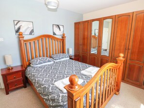 A bedroom with a wooden bed, a nightstand, a wardrobe, and two wall-mounted mirrors. - Newton West Farm (Haverfordwest)