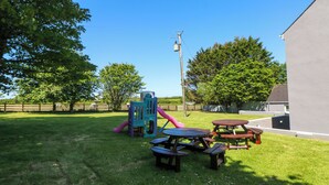 Un espacio al aire libre con césped, mesas de picnic y un parque infantil.