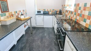 Una cocina compacta con armarios blancos, microondas, tostadora y estufa a gas.