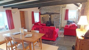 Ein gemütliches Wohnzimmer mit Kamin aus Stein, roten Sofas und einem Holzesstisch.