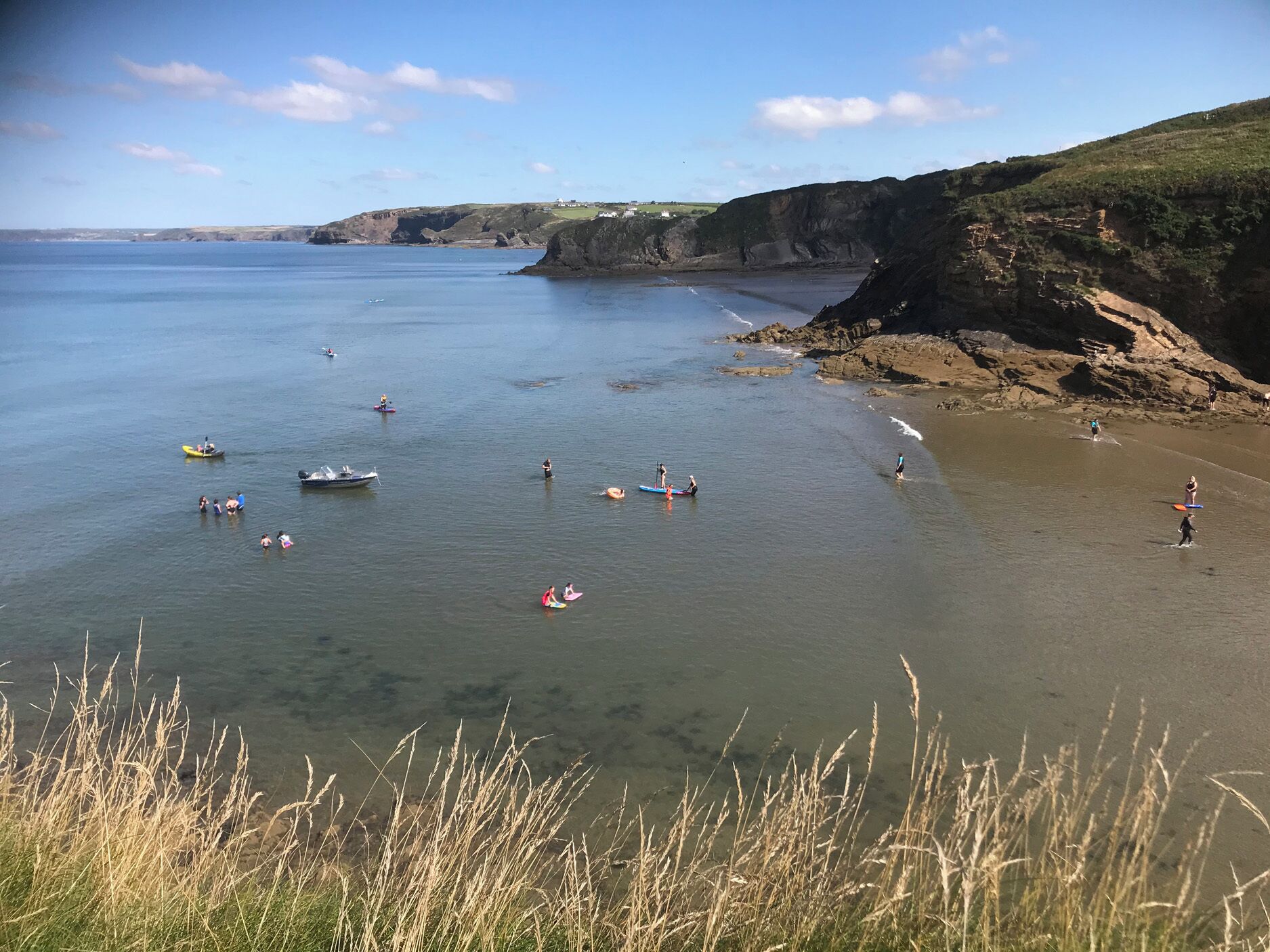 A coastal area with calm waters, boats, and people engaging in water activities.