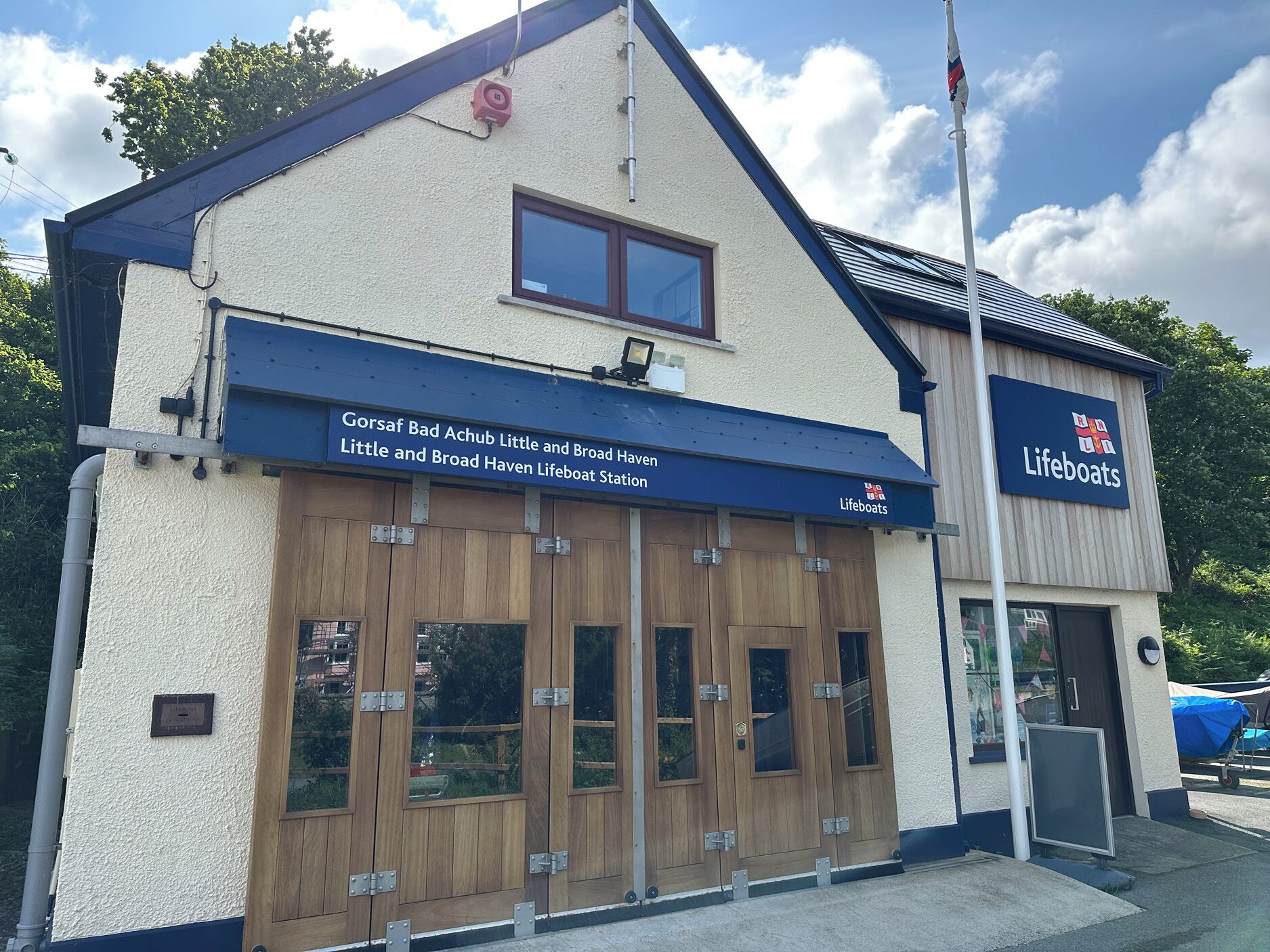 Een gebouw met een bordje voor 'Gorsaf Bad Achub Little and Broad Haven Lifeboat Station' en een bord 'Reddingsboten' aan de rechterkant.