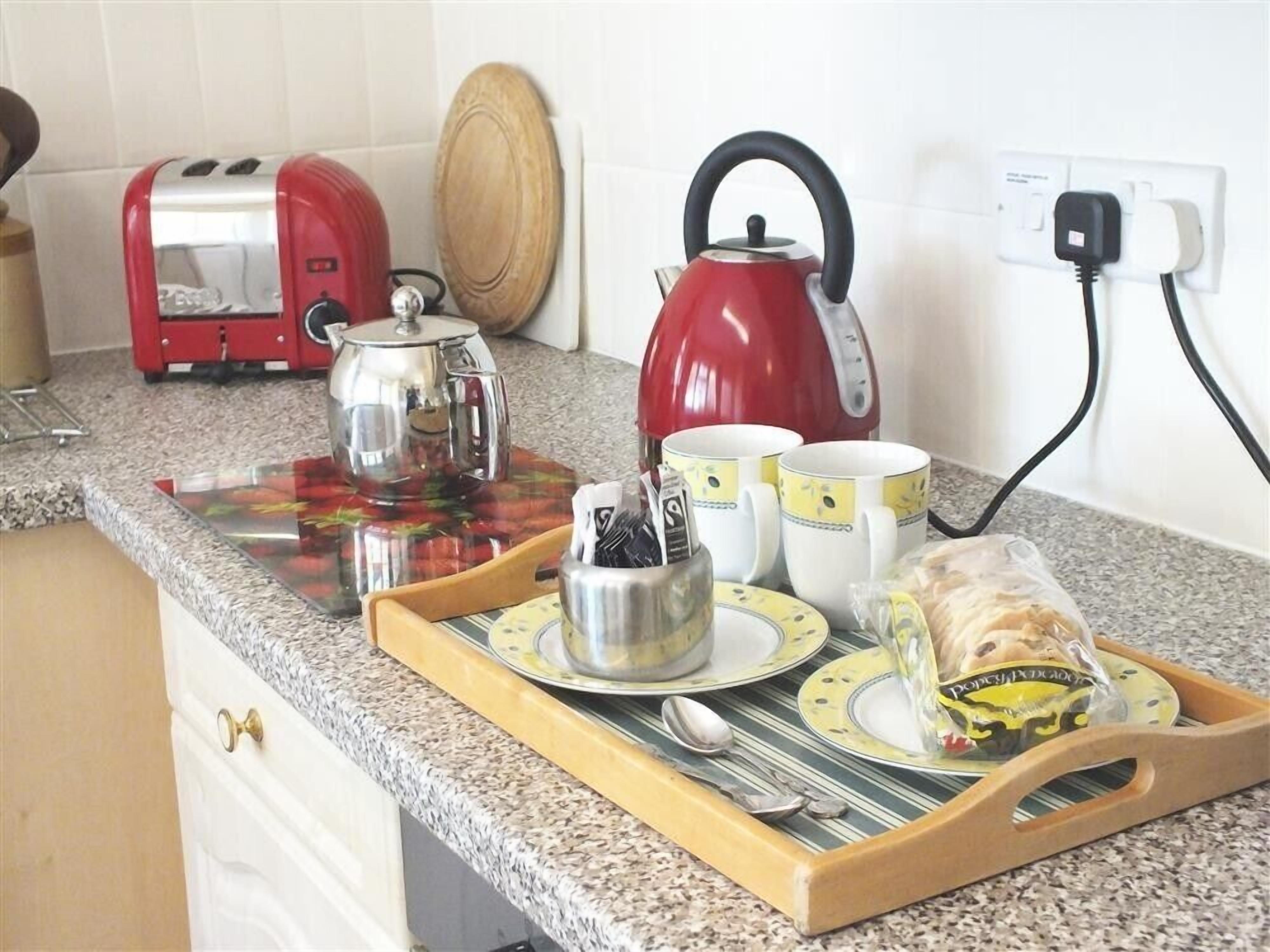 A kitchen counter with a toaster, kettle, teapot, cups, plates, and a tray with utensils and a loaf of bread.