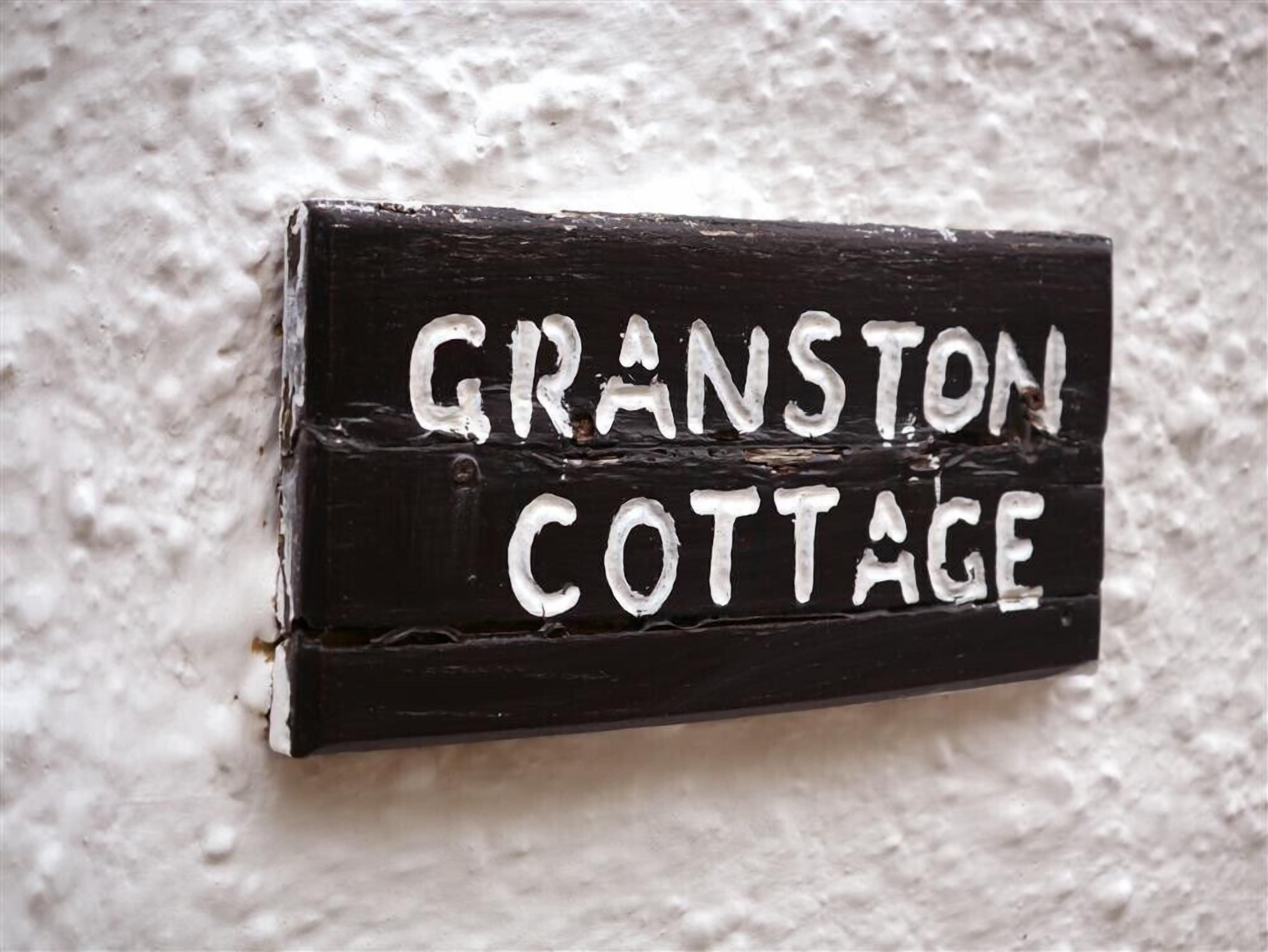 Un letrero negro con letras blancas que dice "GRANSTON COTTAGE" montado en una pared con textura.
