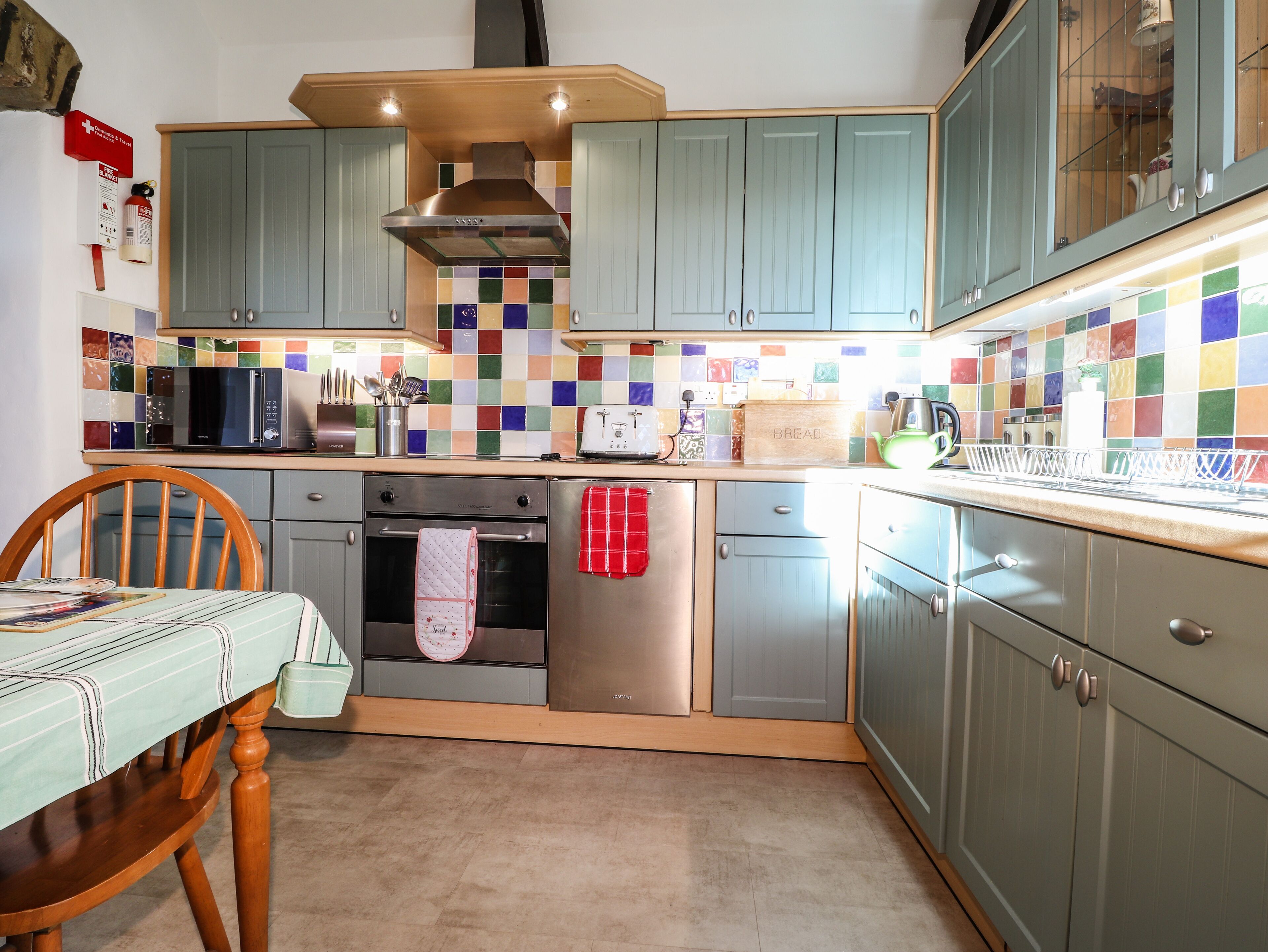 A kitchen with teal cabinets, a microwave, a toaster, and a colorful tiled backsplash.