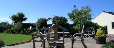 A patio with stone flooring, wooden furniture, and a large wooden wheel.