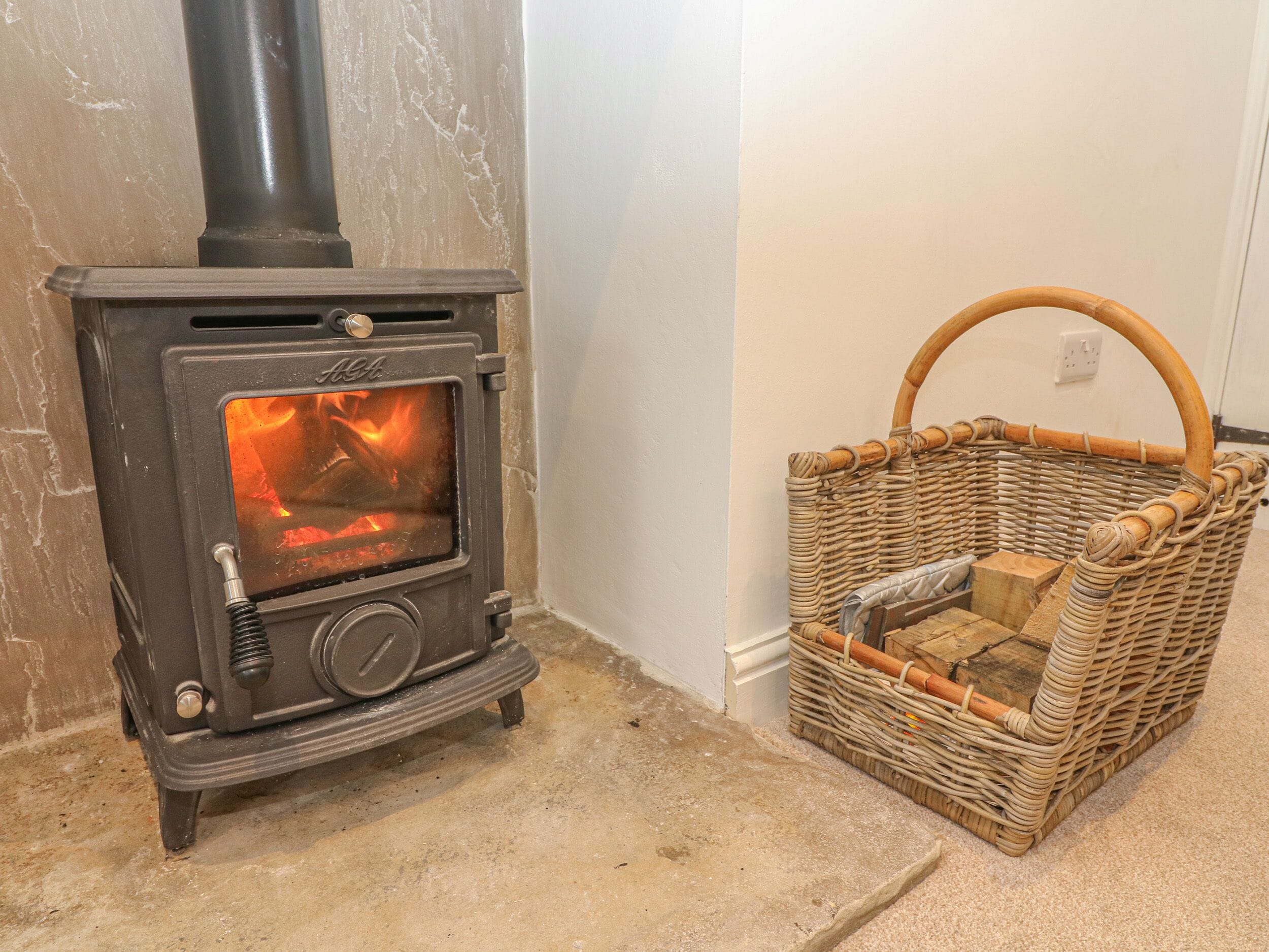 A wood-burning stove with a basket next to it.