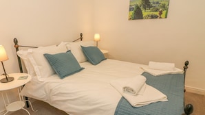 A neatly made bed with white and blue bedding, two bedside lamps, and a painting of a landscape on the wall. - The Little Bower (Hawes)