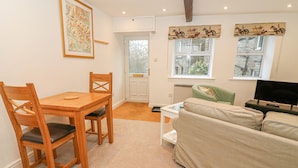 A living room with a wooden dining table, green armchair, beige sofa, and a television. - The Little Bower (Hawes)