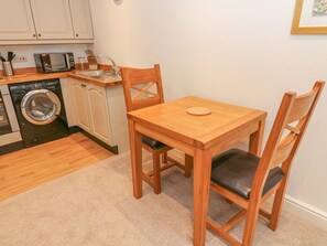 A compact kitchen with a microwave, sink, and washing machine. There is a wooden table with two chairs. - The Little Bower (Hawes)
