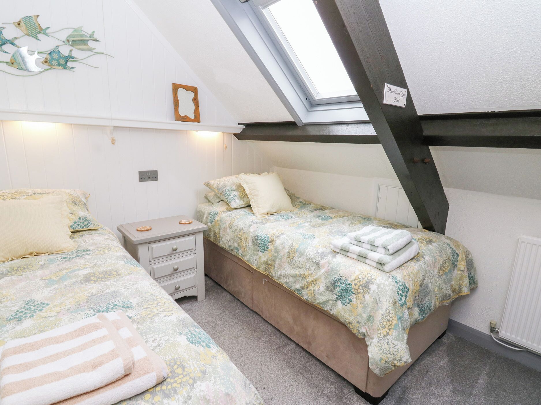 A small, cozy bedroom with two beds, a nightstand, and a skylight.