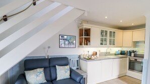 A modern kitchen with white cabinets, a built-in oven, and a dining area with a blue sofa and decorative pillows. - 5 The Coach House (Haverfordwest)