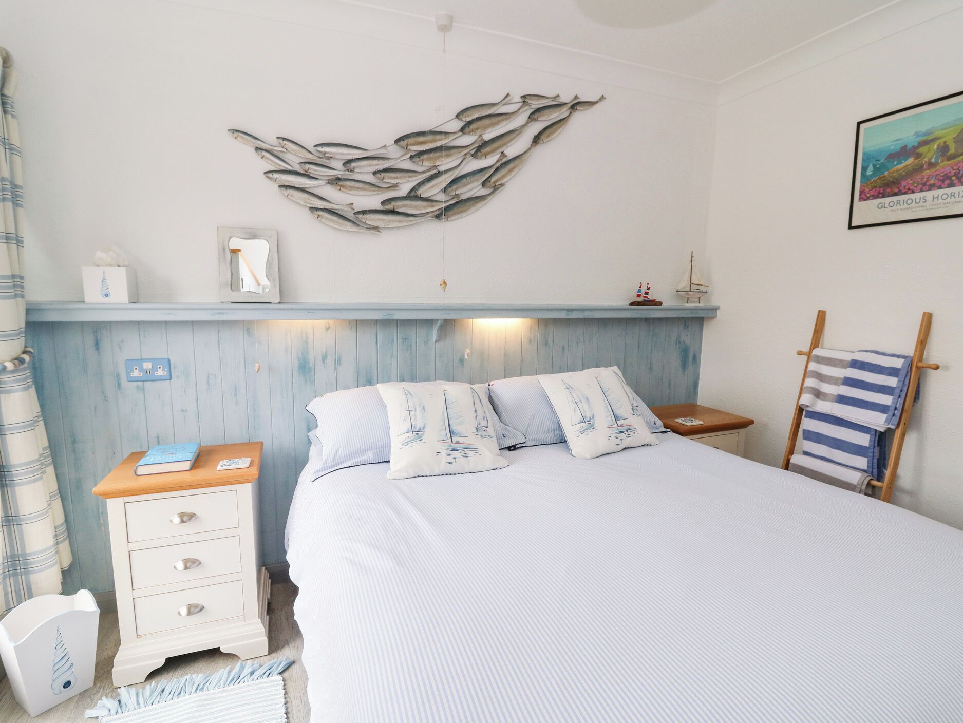 A bedroom with a bed, a nightstand, a dresser, a wall-mounted shelf, a towel rack, and a decorative fish wall art piece.