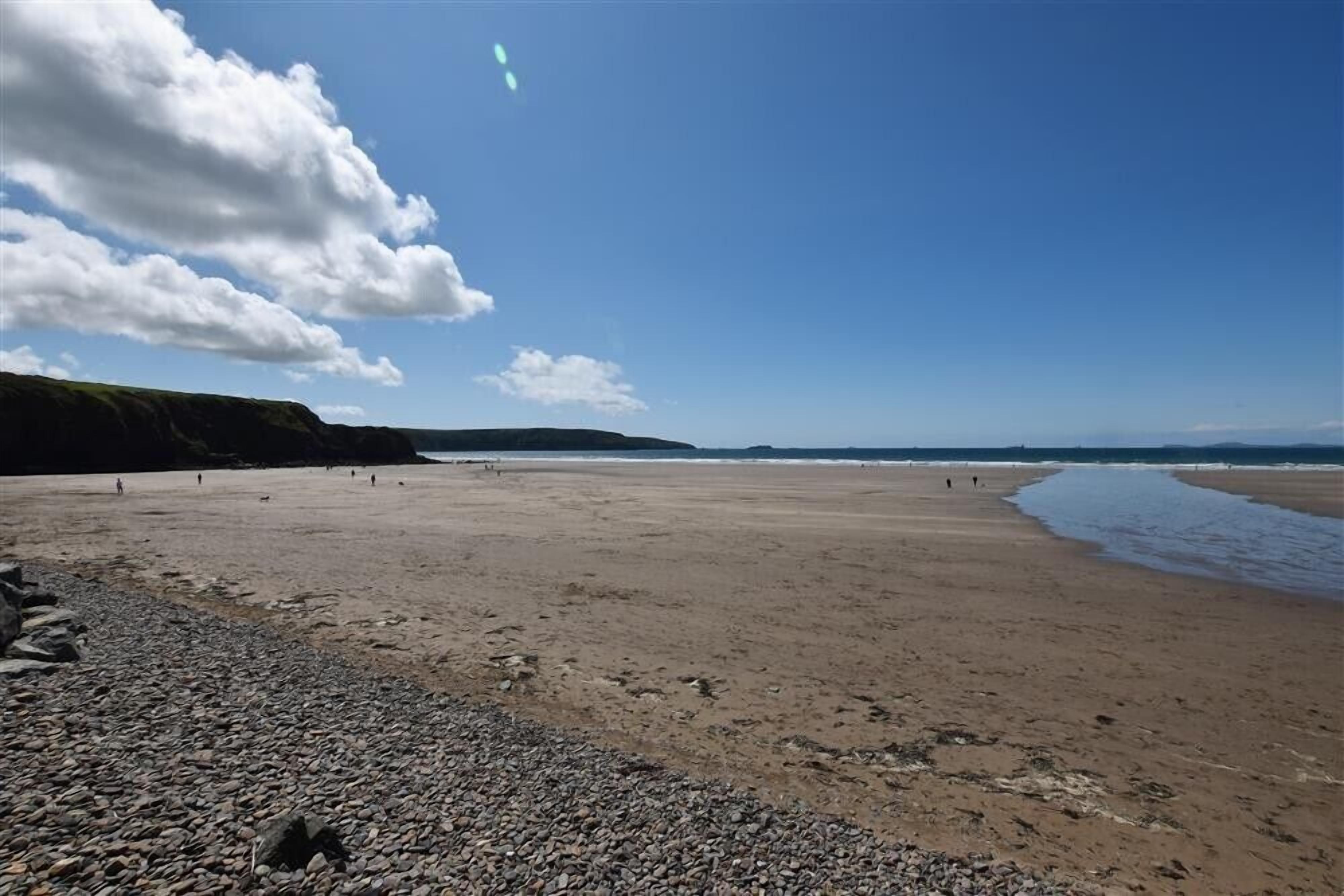A wide, pebbly beach with a clear sky and distant hills.