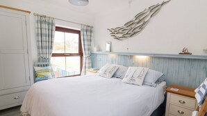 A bedroom with a bed, bedside tables, a window with curtains, a wall-mounted light fixture, and a small shelf with decorative items. - 5 The Coach House (Haverfordwest)