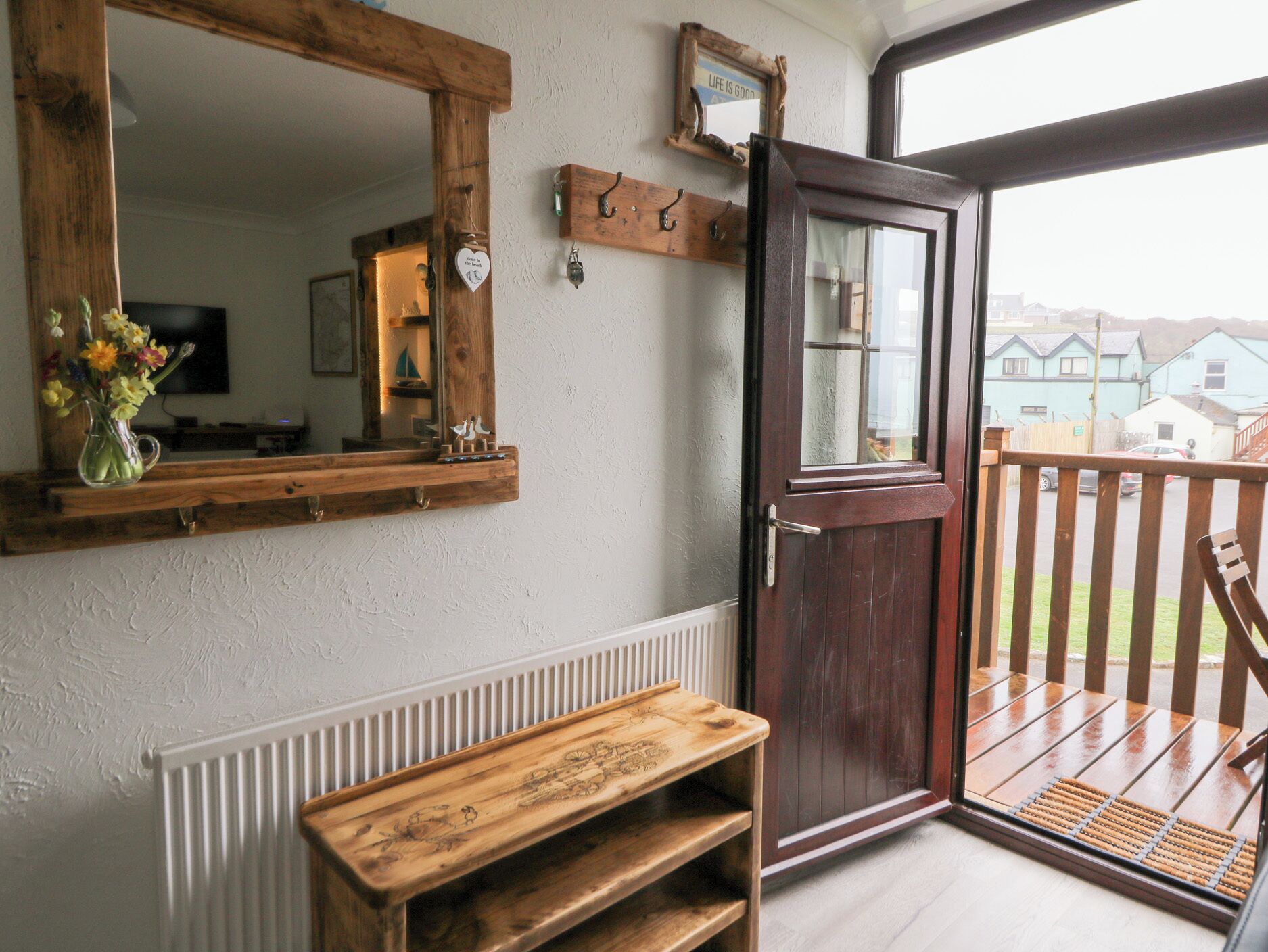A wooden bench, a mirror, and a door with a view of a balcony and houses outside.