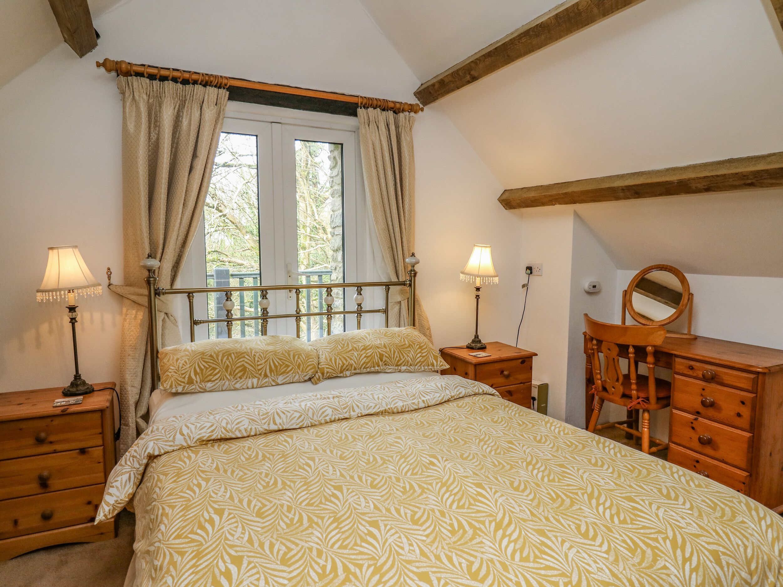 A bedroom with a large bed, two bedside tables with lamps, a wooden dresser, and a window with curtains.