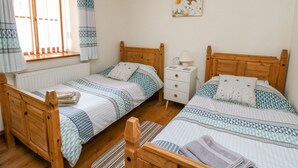 A bedroom with two wooden beds, a nightstand, a radiator, and a window with curtains. - Beudy (Cardigan)
