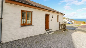 A white building with a wooden door and windows, a gravel driveway, and a view of the sea. - Beudy (Cardigan)