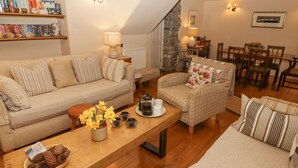 Ein gemütliches Wohnzimmer mit Sofa, Sessel und Couchtisch, ausgestattet mit Bücherregalen und einem Essbereich.