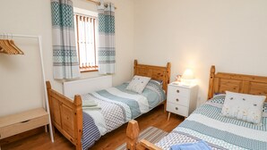 Una camera da letto con due letti in legno, un comodino con una lampada, un armadio in legno e una finestra con tende a motivi.