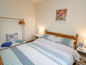 A neatly arranged bedroom with a large bed, a bedside table with a lamp, a chair with a floral cushion, and a wall-mounted artwork. - Llaethdy (Cardigan)