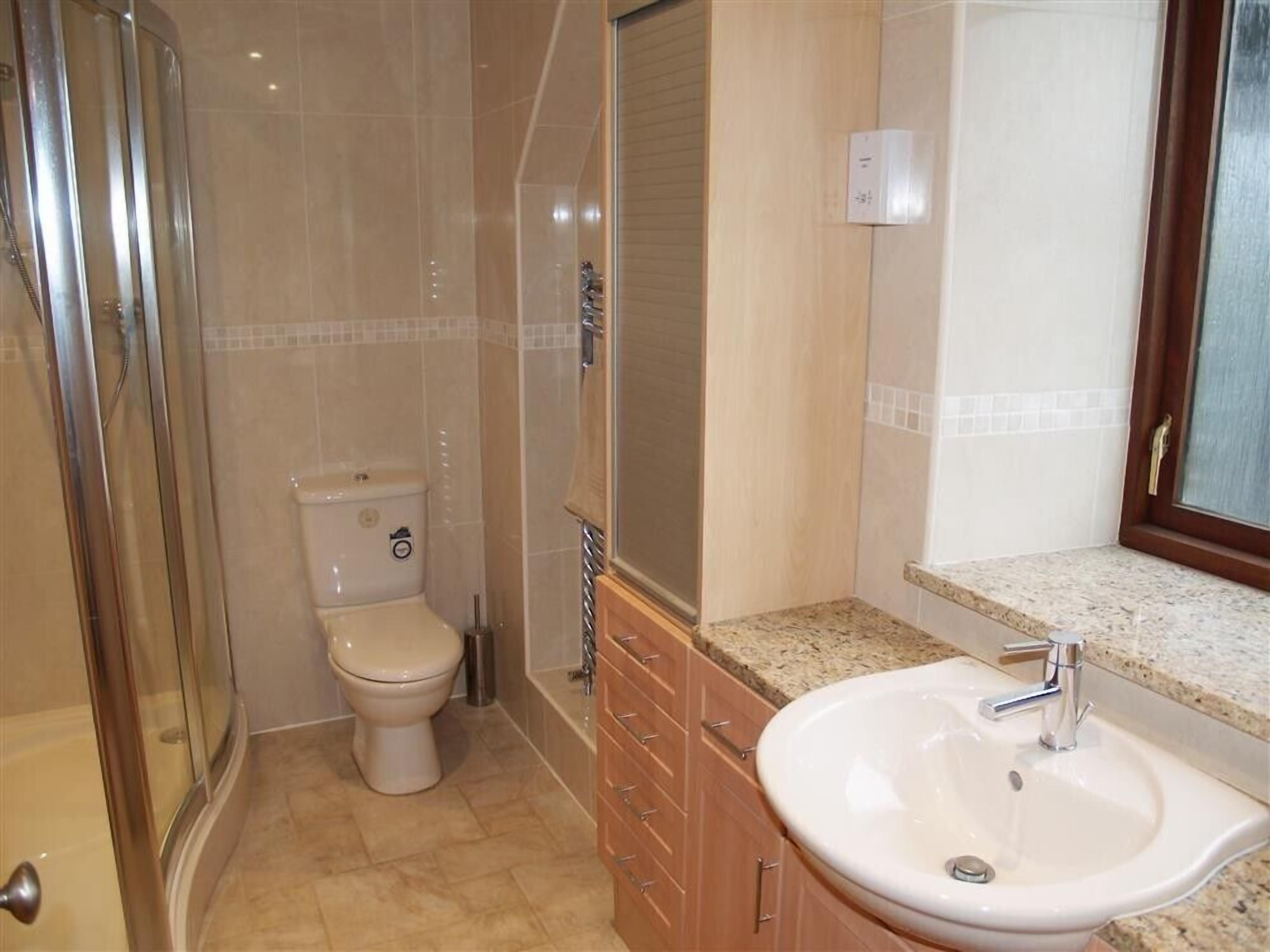 A bathroom with a glass-enclosed shower, a toilet, a sink with a countertop, and wooden cabinets.