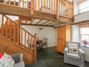 A wooden staircase leading to a loft area with a dining table and chairs, a striped armchair, and a wooden cabinet. - West End Cottage (Newport)