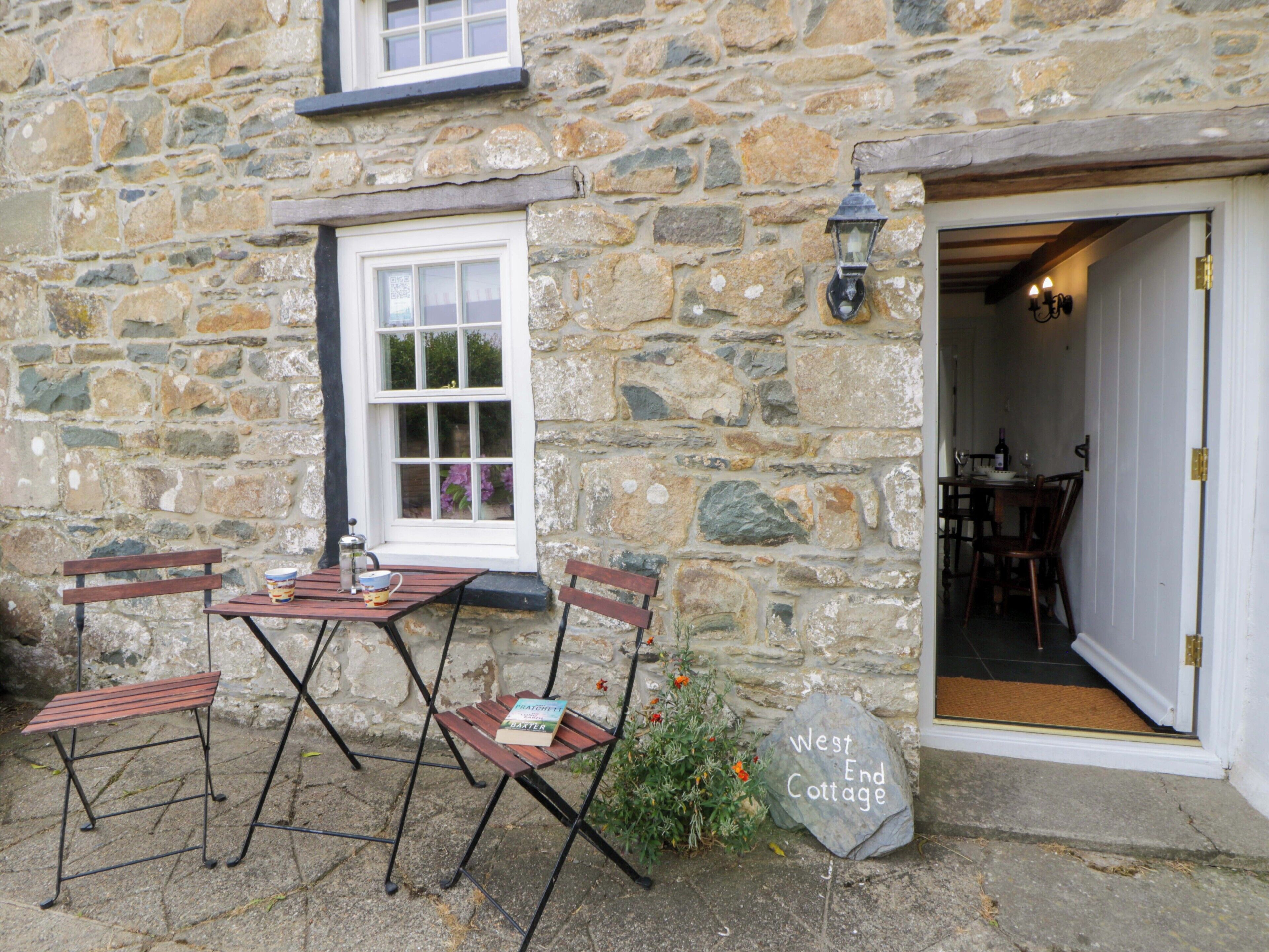 Une maison de campagne en pierre, avec une table et des chaises en bois, une fenêtre et une porte donnant sur l’intérieur.