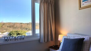 A bedroom with a window, a bed, a nightstand, and a lamp.