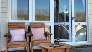 A wooden bench with a cup and a French press on a table outside a house with large windows and a door marked with the number 34.