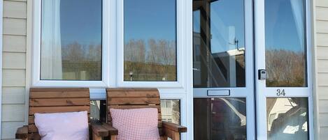 Un banco de madera con una taza y una prensa francesa sobre una mesa frente a una casa con ventanas grandes y una puerta con el número 34.