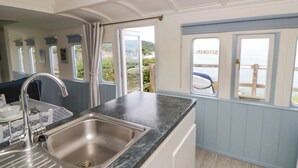 Een keuken met een roestvrijstalen spoelbak, een raam met uitzicht op zee, en een deur naar buiten.