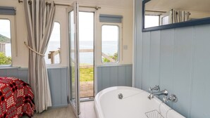 Een slaapkamer met een groot bad, een raam met gordijnen en uitzicht op zee.