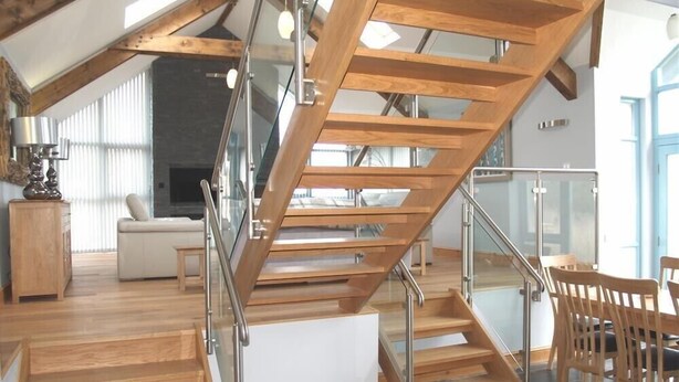 A modern interior with a wooden staircase, glass railings, and a living area with a sofa and chairs. - Seabrook (Haverfordwest)