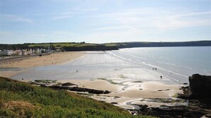 A coastal beach with a clear sky, sandy shore, and buildings in the background. - Seabrook (Haverfordwest)