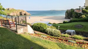A coastal view with a beach, a garden with colorful flowers, and a stone structure in the background. - Gwyddno Lodge (Narberth)