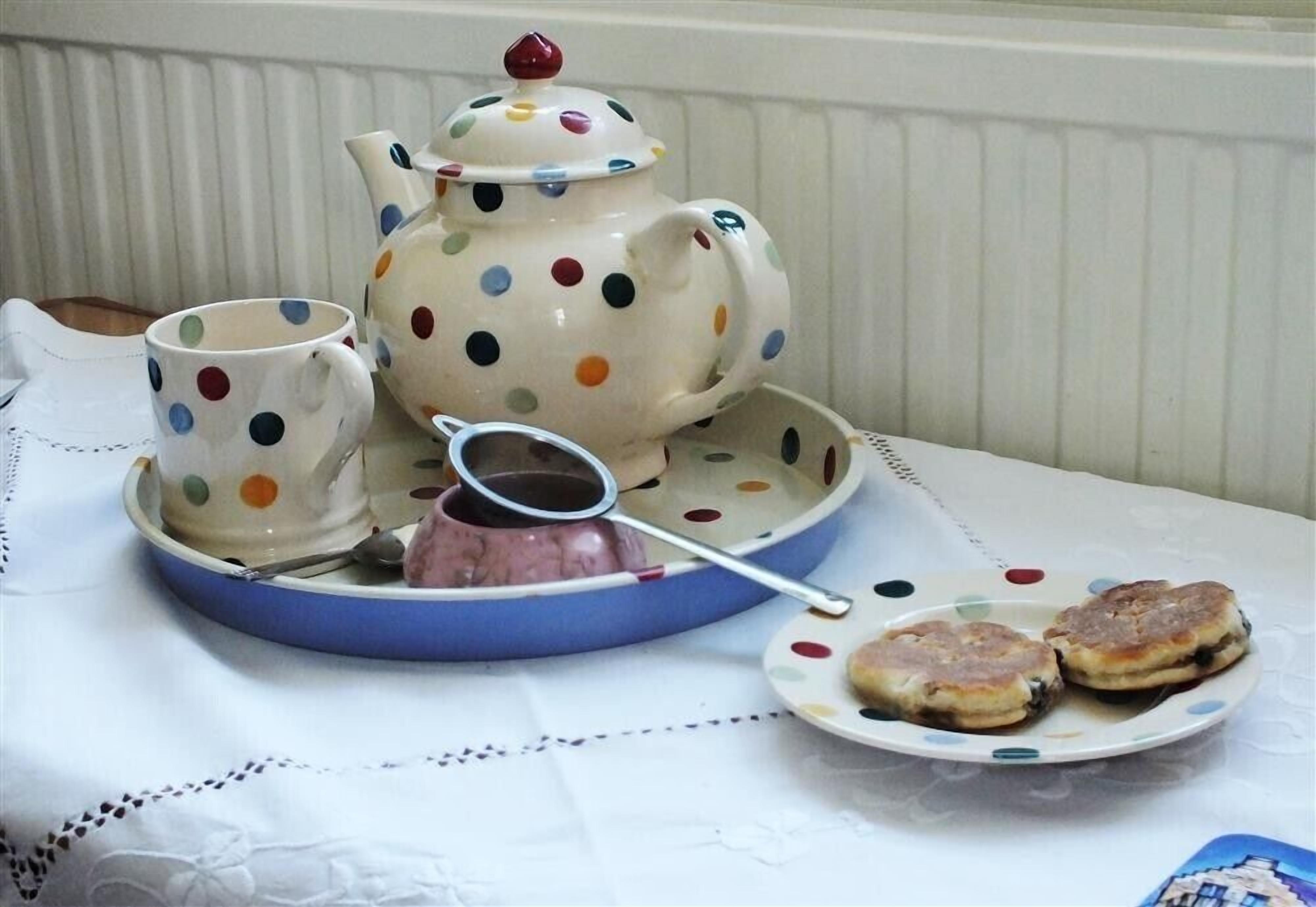 A table set with a polka-dotted teapot, a matching cup, a teapot strainer, and two pastries on a plate.