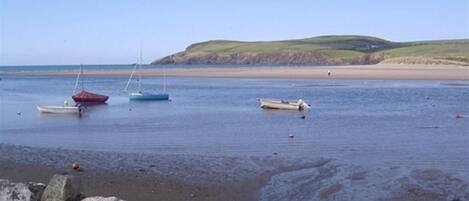 A coastal scene with boats on calm water, a sandy beach, and a stone wall in the foreground.