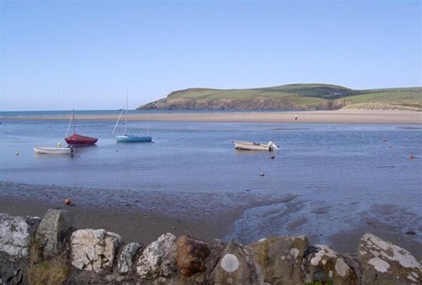 A coastal scene with boats on calm water, a sandy beach, and a stone wall in the foreground.