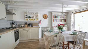 Cozinha com mesa de jantar, cadeiras, relógio e estante.