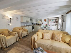 A cozy living room with two sofas and a coffee table, a kitchen with white cabinets, and a bookshelf filled with books. - End Cottage (Newport)