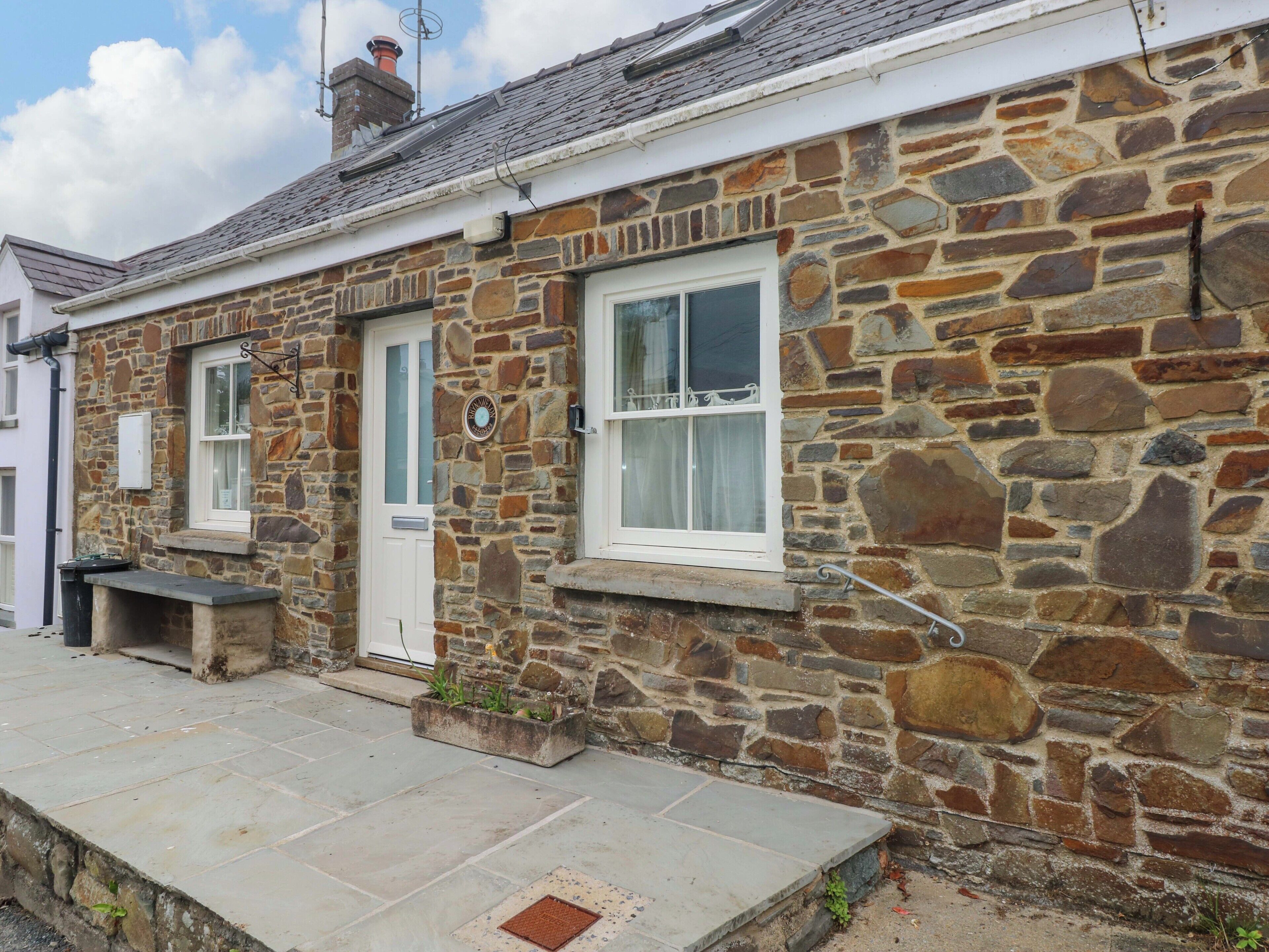 A stone building with a white door, two windows, and a small outdoor seating area.