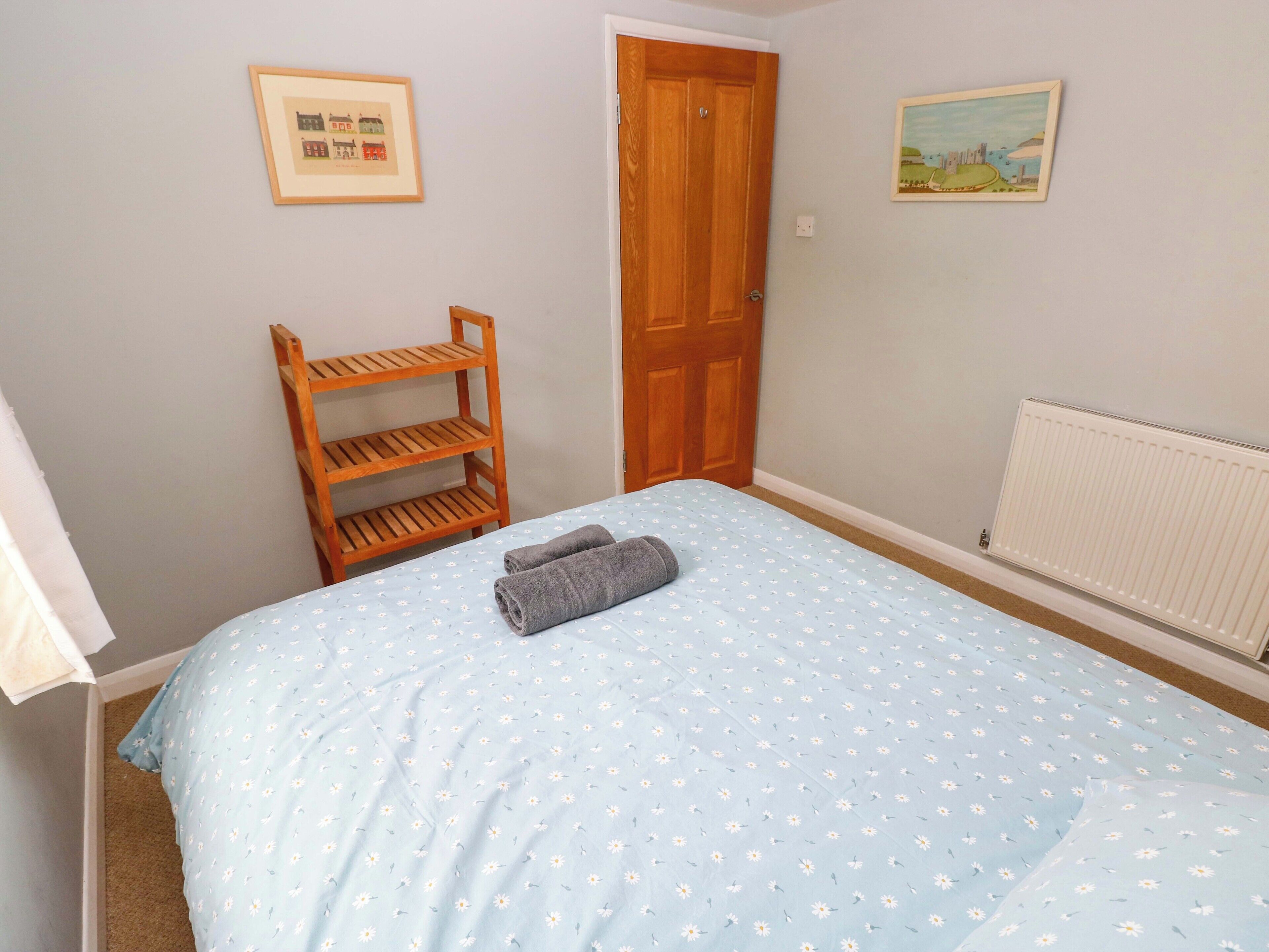 Une chambre à coucher avec un lit, une étagère en bois, une porte et deux tableaux encadrés accrochés au mur.