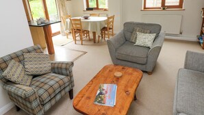 Een woonkamer met een geruite bank, een grijze fauteuil, een houten salontafel en een eethoek met een tafel en stoelen.