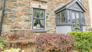 A stone building with a bench outside, a window with curtains, and a sign that reads "Greenbanks". - Greenbanks (Newport)