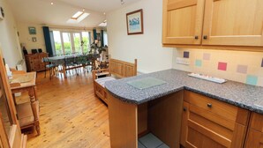 A kitchen with wooden cabinets, a granite countertop, and a dining area with a table and chairs. - Greenbanks (Newport)