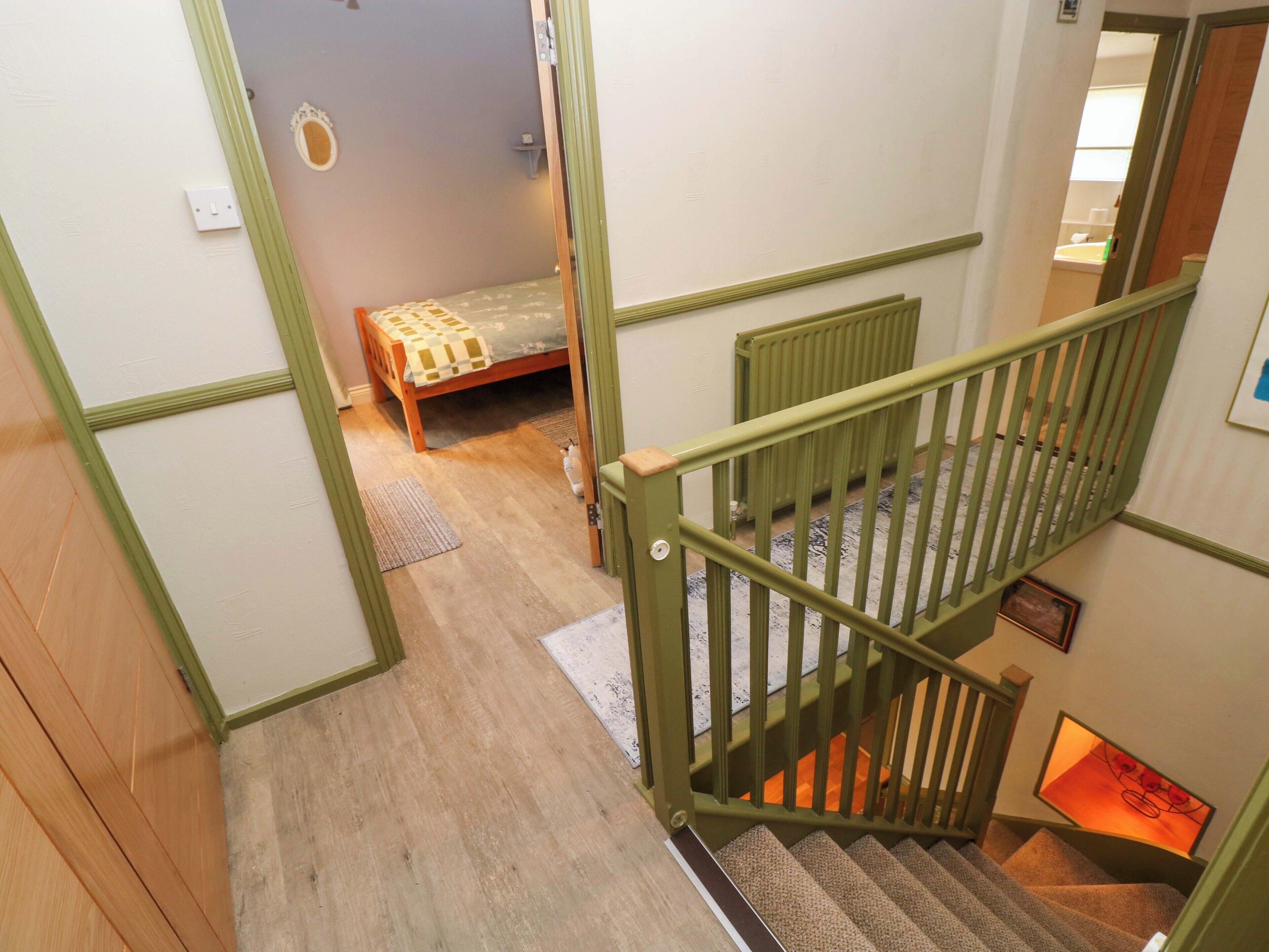 Een trap met een groene leuning die leidt naar een slaapkamer met een bed en een radiator.