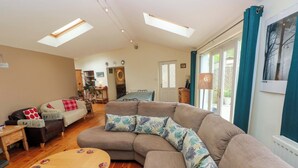 A living room with a sectional sofa, a round wooden coffee table, and a dining area in the background. - Greenbanks (Newport)