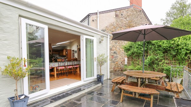 A patio with a wooden table and benches, a potted plant, and a large umbrella. - Greenbanks (Newport)